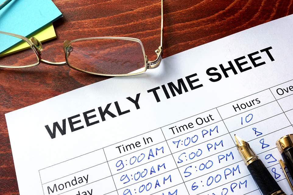 A paper printed weekly time sheet filled with time in and time out times and worked hours inside the time sheet written by hand with a pen